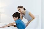 Little boy using computer keyboard, mother watching over his shoulder