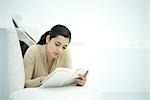 Young woman lying on couch, reading book