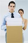 Young office workers, young man holding stack of paper on cardboard box, looking at camera