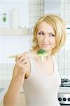 Femme blonde tenant un morceau de brocoli avec des baguettes