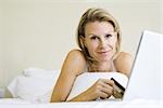 Femme allongée sur le lit, à l'aide de cartes de crédit et portable, souriant à la caméra