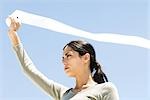 Woman holding up toilet paper roll outdoors, paper streaming in wind, low angle view