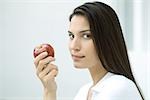 Woman holding apple, looking sideways at camera