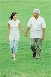 Grandfather and teen granddaughter walking outdoors, holding hands, smiling at each other