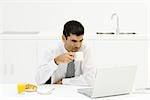 Homme assis à la table de la cuisine, à la recherche à l'ordinateur portable, boire du café