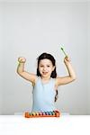 Little girl playing xylophone, arms raised, looking at camera