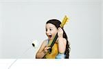 Little girl playing guitar, making face as flower leans toward her