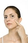 Woman pointing at plastic surgery markings on cheek, looking at camera