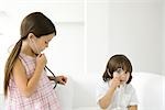 Little boy looking through magnifying glass at camera, girl listening to stethoscope