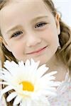 Tête de jeune fille souriant à la caméra, tête penchée, fleurs au premier plan