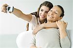 Teen girl photographing self and grandmother with photophone, both smiling