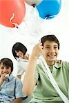 Boy holding helium balloons, smiling, mother and brother in background