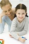 Little girl sitting on mother's lap, coloring, smiling at camera