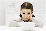 Little girl sitting in front of bowl, holding head, sulking