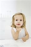 Little girl at table, holding bread in hand, looking up