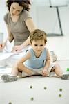 Boy playing with marbles while young mother uses phone and looks at paperwork in background