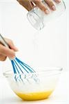 Hand holding whisk, pouring flour into mixing bowl