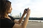 Young man photographing waterfront with digital camera, side view