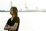 Young man standing along waterfront, arms folded, looking away