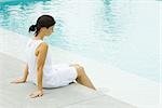 Frau sitzt am Rand des Pools, baumeln die Füße im Wasser, Seitenansicht