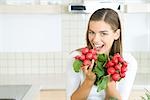 Woman holding up bunches of fresh radishes, smiling at camera