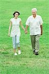 Grandfather and teen granddaughter walking outdoors, holding hands, smiling at camera
