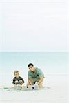 Père et fils, faire des châteaux de sable sur la plage, souriant à la caméra