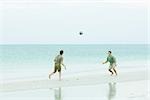 Father and teen son at the beach, both looking up at ball in midair