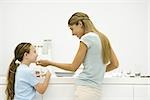 Mother and daughter in kitchen, woman holding girl's chin, both smiling