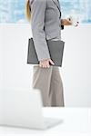 Businesswoman holding disposable coffee cup and folders, side view, cropped