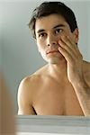 Bare-chested man looking at self in mirror, touching face