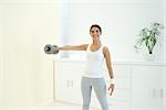 Young woman lifting weights at home, smiling at camera