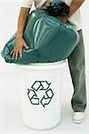 Man forcing large garbage bag into recycling bin, cropped view