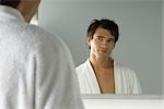 Man in bathrobe smiling at self in mirror