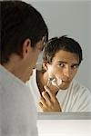Man shaving, looking at self in mirror
