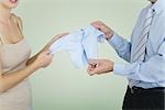 Couple holding up baby clothing together, cropped view