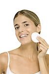 Woman wiping face with cotton cosmetic pad, smiling at camera