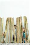 Father and two children peeking through bamboo at camera, all smiling