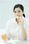 Junge Frau Essen Croissant, sitzen am Schreibtisch, Blick in die Kamera