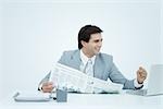 Young businessman looking at laptop and smiling, holding newspaper and clenching fist