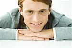 Young man resting head on folded arms, smiling at camera, portrait