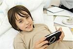 Boy holding handheld video game, lying down and smiling at camera