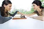 Two women playing chess, one making a move, the other touching her hand