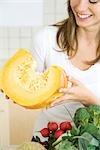 Woman holding large slice of raw pumpkin, smiling