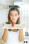 Woman, eyes closed, presenting plate with single raw radish in center