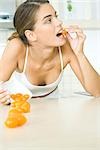 Woman spilling bowl of yellow cherry tomatoes, leaning on elbow, biting into one