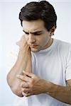 Man putting adhesive bandage on arm, frowning