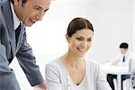 Professional man leaning over woman's shoulder, both looking down and smiling