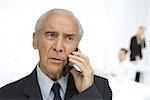 Senior businessman using cell phone, furrowing brow