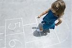 Little girl playing hopscotch outdoors, overhead view